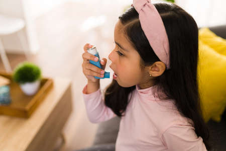 Side view of a cute little girl with breathing problems using an asthma inhalerの写真素材