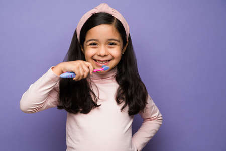 Dental hygiene. Cheerful girl enjoying brushing her teeth and smiling after eating breakfastの写真素材