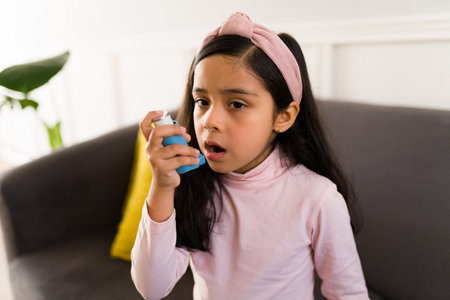 Beautiful elementary girl having an asthma attack and using an inhaler while at home