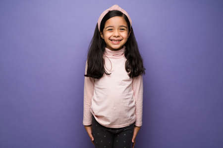 I'm so happy. Cheerful little girl wearing casual clothes and smiling against a purple studio backgroundの写真素材