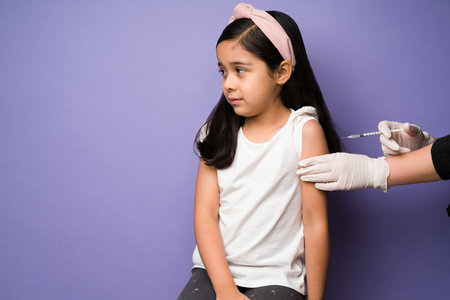 Scared little kid feeling in pain while getting the shot for the vaccine in front of a purple...