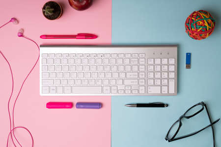 His and her office desk. Pink and blue workspace with a computer keyboard, headphones, eyeglasses, and paper markersの写真素材