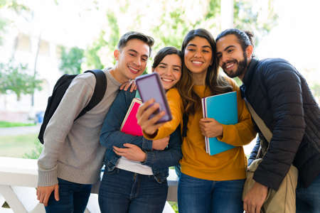 Posting on social media. Cheerful young woman taking a selfie with her college friendsの写真素材