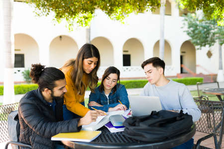 Study group sitting outside at university. Smart student explaining the homework to her college friends and doing research on the laptopの写真素材