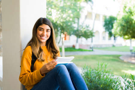 Smart college girl making eye contact and smiling while studying for her exam before class