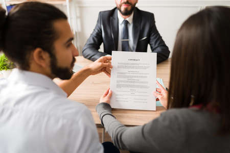 Rear view of an hispanic couple reading the contract and signing a business agreement with a finance consultantの写真素材
