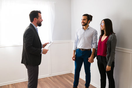 Real estate agent showing a house to a happy hispanic woman and man. Interested couple looking to buy a new propertyの写真素材