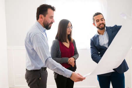Attractive couple visiting a model home and looking at the construction plans with a real estate agentの写真素材