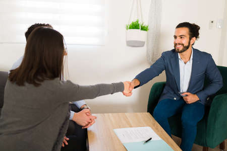 Attractive finance consultant shaking hands with a couple of clients at their home to offer them credits and investmentsの写真素材