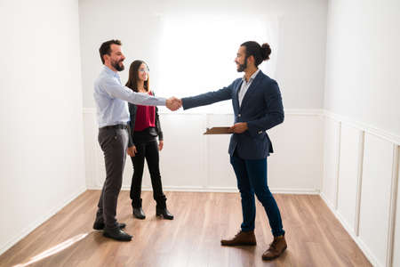 This is the new home for you. Hispanic realtor shaking hands with new clients doing a property tour in a new homeの写真素材