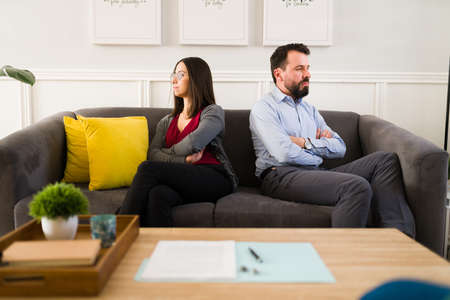 I hate you. Upset latin woman and man signing the divorce papers and ignoring each other after while sitting on the couchの写真素材