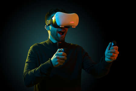 Cheerful young man playing a fun video game while using a virtual reality headset with controllers
