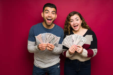 We won a lot of money! Surprised young couple holding a lot of cash and looking excited after winning the lotteryの写真素材