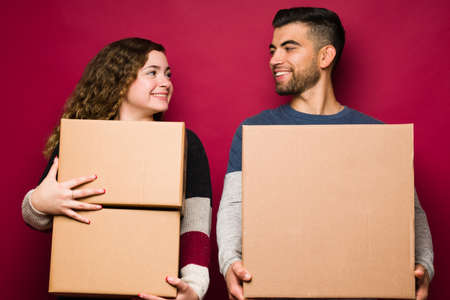 Beautiful woman moving in with her boyfriend while carrying boxes. Happy couple moving to a new house or apartmentの写真素材