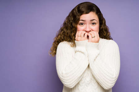 Scared young woman biting her nails while feeling anxious and afraid after watching horror movies aloneの写真素材