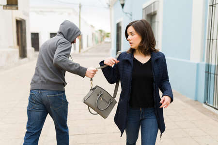 Oh no! Rear view of a thief criminal stealing the purse from a scared young woman during broad daylight on the streetの写真素材