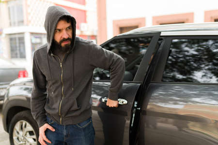 Committing carjacking. Young man in his 30s and car thief trying to steal a new car on the streetの写真素材
