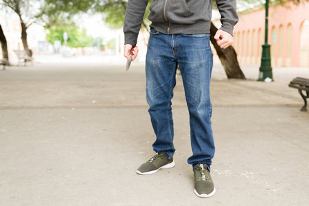 Ready to fight. Young man and criminal thief holding a knife on the park while waiting to steal...
