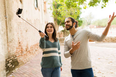 Making an online reel. Attractive woman and man doing a live stream using a selfie stick with a smartphone at the parkの写真素材