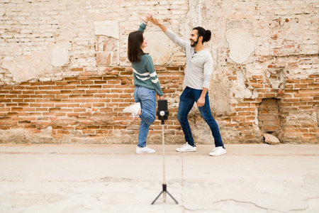 Happy centennial couple filming themselves dancing together on a smartphone to share on a social media platformの写真素材