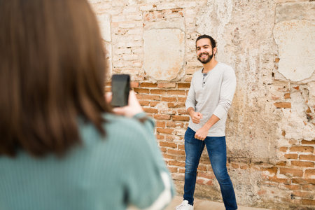 Rear view of a woman filming a cheerful gen z man dancing a viral song outdoors to share on a social...