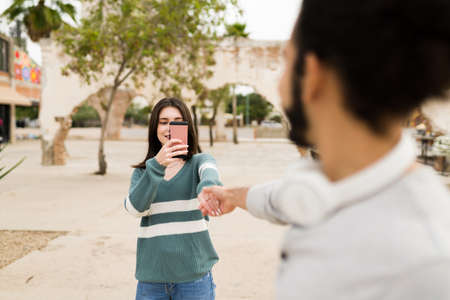 I want to be with you always. Adorable woman holding hands with her boyfriend and taking a photo using a smartphoneの写真素材