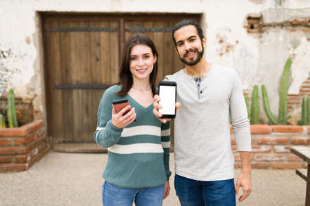 Portrait of an attractive gen z couple texting and showing their smartphone screen while using...