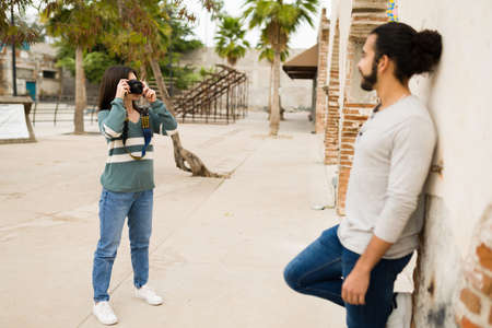 Loving girlfriend taking photos of her boyfriend with a camera during a casual photoshoot at the parkの写真素材