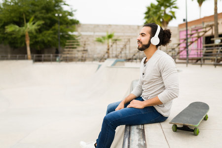 Side view of a relaxed young man listening to music with wireless headphones and skateboarding at the parkの写真素材