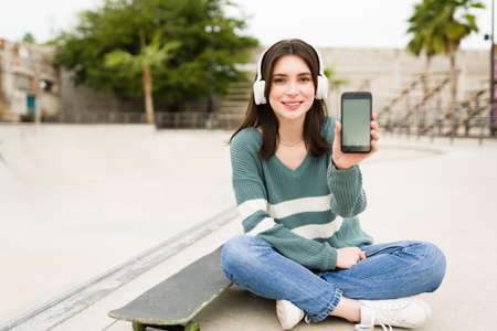 Portrait of a gorgeous young woman showing her smartphone screen while texting and using social media at the skate parkの写真素材