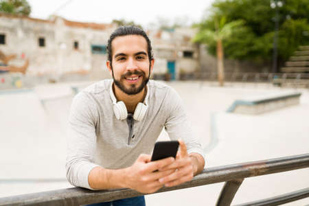 Good-looking young man using social media on the smartphone and smiling while relaxing outdoors