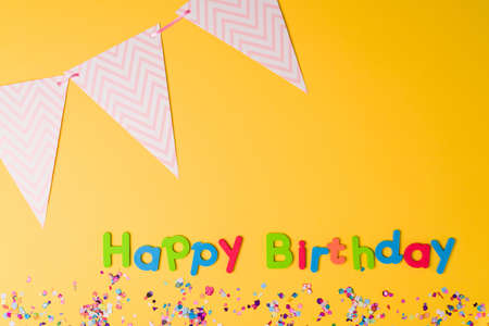 Studio shot of a colorful happy birthday with confetti and party items against a bright yellow backgroundの写真素材