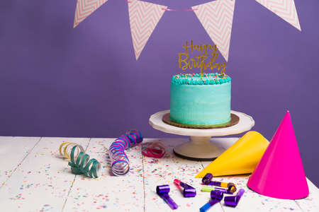 Celebrating a birthday party! White table with a delicious cake and a happy birthday sign surrounded...