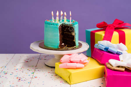 Chocolate cake with delicious blue icing and lit candles next to beautiful presents for a party celebrationの写真素材
