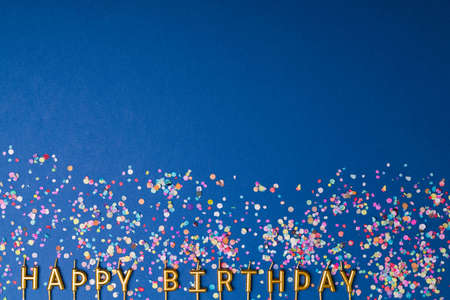 Celebrating a party. Studio shot of gold happy birthday candles with colorful confetti on a blue...