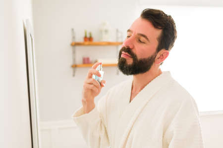 I'm going out on a date. Handsome young man wearing a white robe putting on a nice fragrance sprayの写真素材