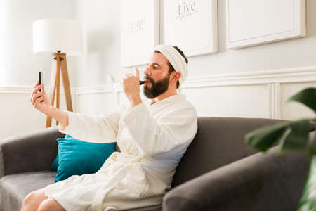 Posting about my day on social media. Attractive man drinking wine and having a relaxing day during a spa at  homeの写真素材