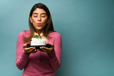 Blowing the birthday candles. Attractive young woman making a wish while holding a delicious cake next to copy spaceの写真素材