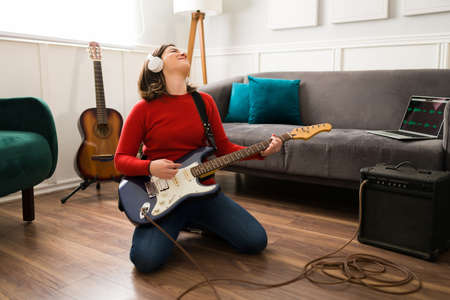 Music is life. Cheerful young woman enjoying and feeling the music while playing the electric guitar connected to an amplifierの写真素材