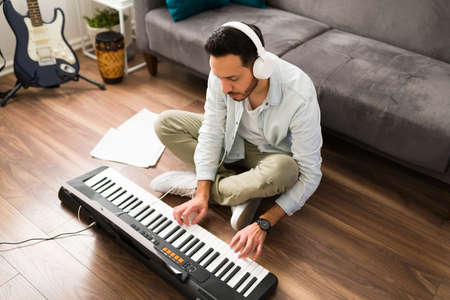 High angle of a musician playing the keyboard and rehearsing new music. Songwriter learning a new...