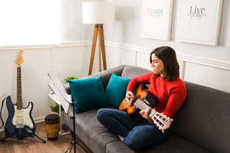 Beautiful woman learning and rehearsing a song on the guitar. Female musician composing new musicの写真素材