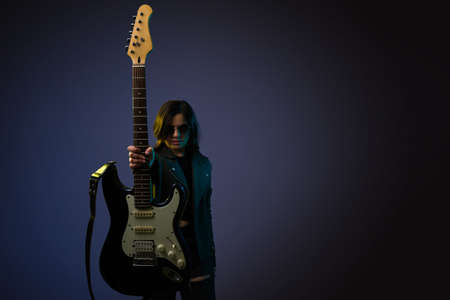 Beautiful young woman showing her black electric guitar. Rock and roll guitarist and singer next to...
