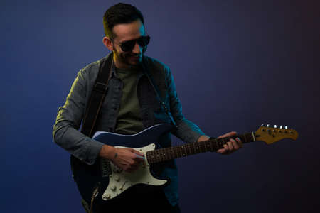 Cheerful young man smiling while playing the electric guitar and getting ready for a performance...