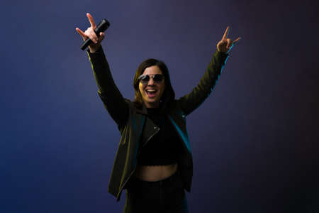 Portrait of an excited young woman putting her arms up. Rock singer screaming to the audience on a concertの写真素材