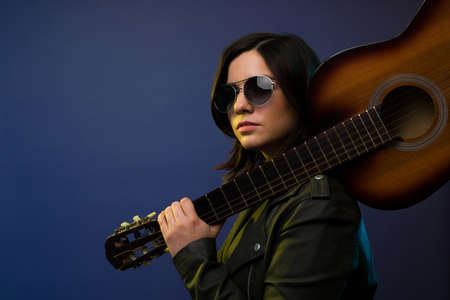Close up of a female guitarist and singer with black sunglasses making eye contact carrying an acoustic guitarの写真素材