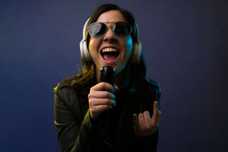 Hard rock music. Close up of an attractive female singer with headphones making the rock and roll sign while singingの写真素材