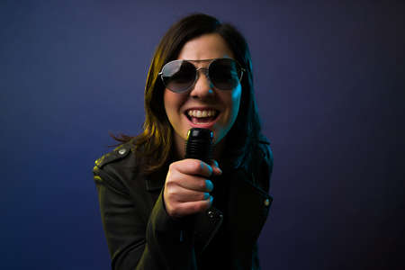 Beautiful artistic woman singing with a microphone and looking at the camera while having funの写真素材