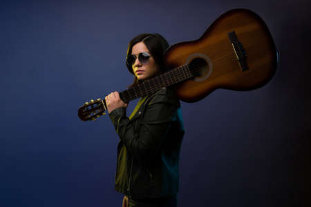 Portrait of an attractive young woman and musician making eye contact while carrying an acoustic guitarの写真素材