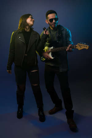 Beatiful young woman singing with a microphone with a guitarist and band member during a rock concertの写真素材