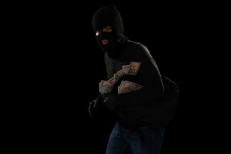 Thief with a black mask breaking into a house and escaping after stealing a lot of money in a backpackの写真素材